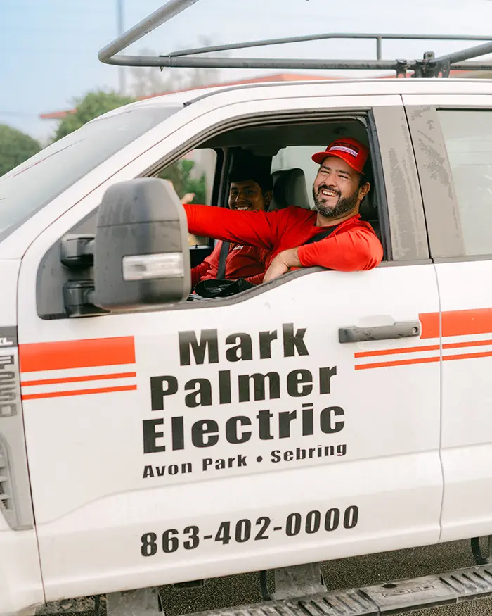 Two Mark Palmer technicians driving a branded truck, smiling at the camera.